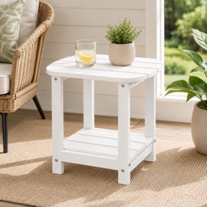 May include: A square white side table with a slatted top and a lower shelf. The table features four sturdy legs with visible silver hardware. A clear ribbed glass containing a yellow liquid and a small potted green plant sit on the surface.