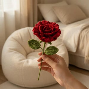 May include: A handmade red crochet rose with green leaves and stem. The rose is in full bloom, showcasing detailed petal work. The leaves are a vibrant green, and the stem is a matching green. This handcrafted floral item is a unique decorative piece.