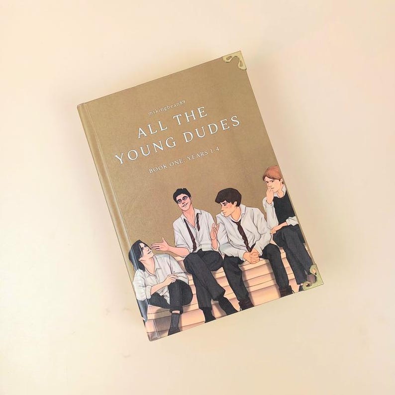 Puede incluir: Un libro de tapa dura titulado "ALL THE YOUNG DUDES" con una ilustraci&oacute;n de cuatro j&oacute;venes. El libro tiene una cubierta de color beige con detalles dorados en las esquinas y texto en una fuente serif. El libro se titula "BOOK ONE YEARS 1-4".
