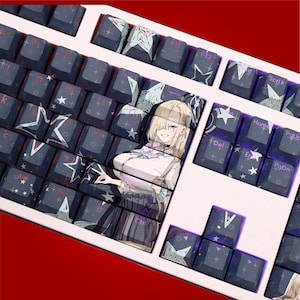 Può includere: Una tastiera meccanica personalizzata con tasti blu scuro con stelle bianche e disegni geometrici. La barra spaziatrice e altri tasti hanno un'illustrazione in stile anime di una donna bionda. La tastiera ha una cornice bianca.