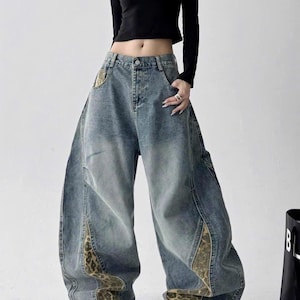 May include: A black long-sleeve crop top paired with wide-leg blue denim jeans. The jeans feature a faded wash, a button and zip fly, and distinct panels of brown and black leopard print fabric integrated along the outer leg seams.