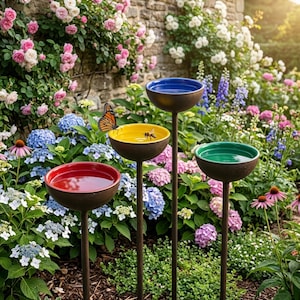 May include: Four bird baths with a brown metal base and bowls in red, yellow, blue, and green. A butterfly rests on the yellow bowl, and a bee is visible. The bird baths are in a garden with flowers.