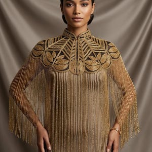 May include: A beige sleeveless dress featuring a high-neck cape overlay. The cape is adorned with intricate gold beadwork in a leaf-like pattern across the shoulders and chest, with long, flowing gold beaded fringe extending down the torso.
