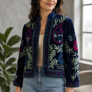 Può includere: Una giacca in velluto blu navy con apertura frontale e colletto alla coreana. Il capo è decorato con intricati ricami floreali e paisley nelle tonalità magenta, verde chiaro e blu lungo i pannelli anteriori e le maniche.