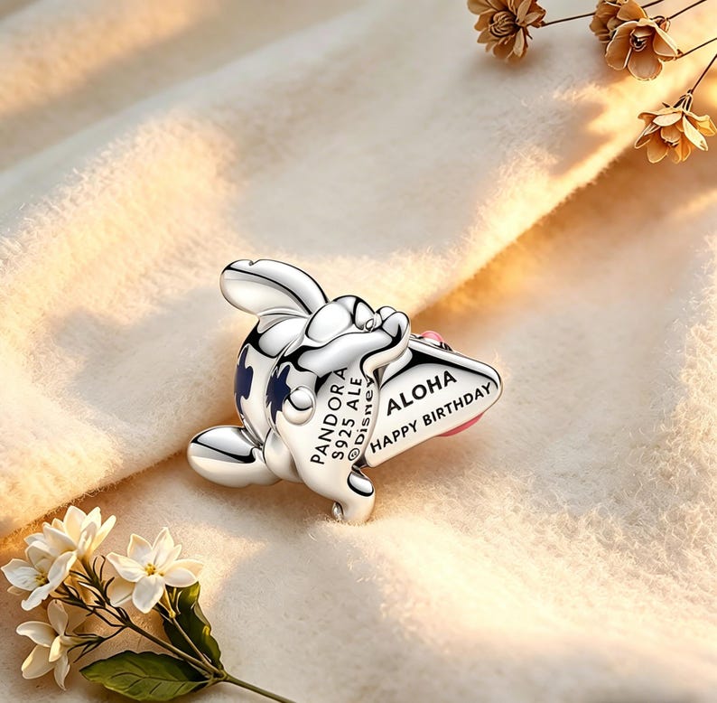 May include: A silver charm depicting a cartoon character with blue details and the words "Aloha Happy Birthday." The charm is from the Pandora Disney collection.