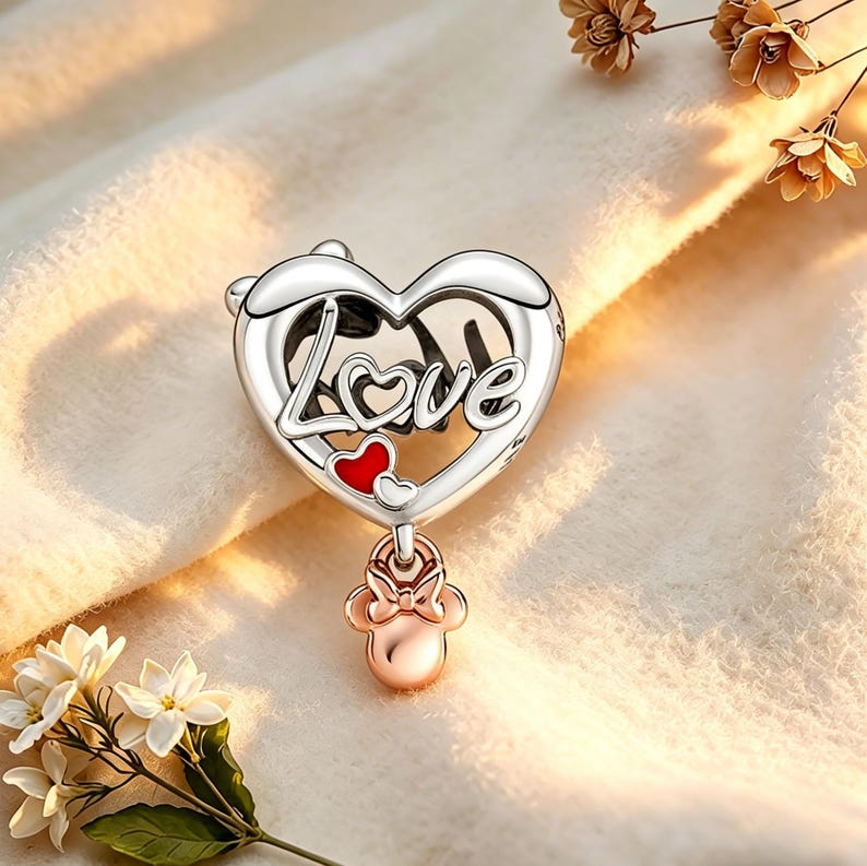 May include: A silver charm with a heart-shaped design. The word "Love" is written across the heart. Two small red hearts are inside the heart. A rose gold charm in the shape of a bow and Minnie Mouse's head hangs below the heart.