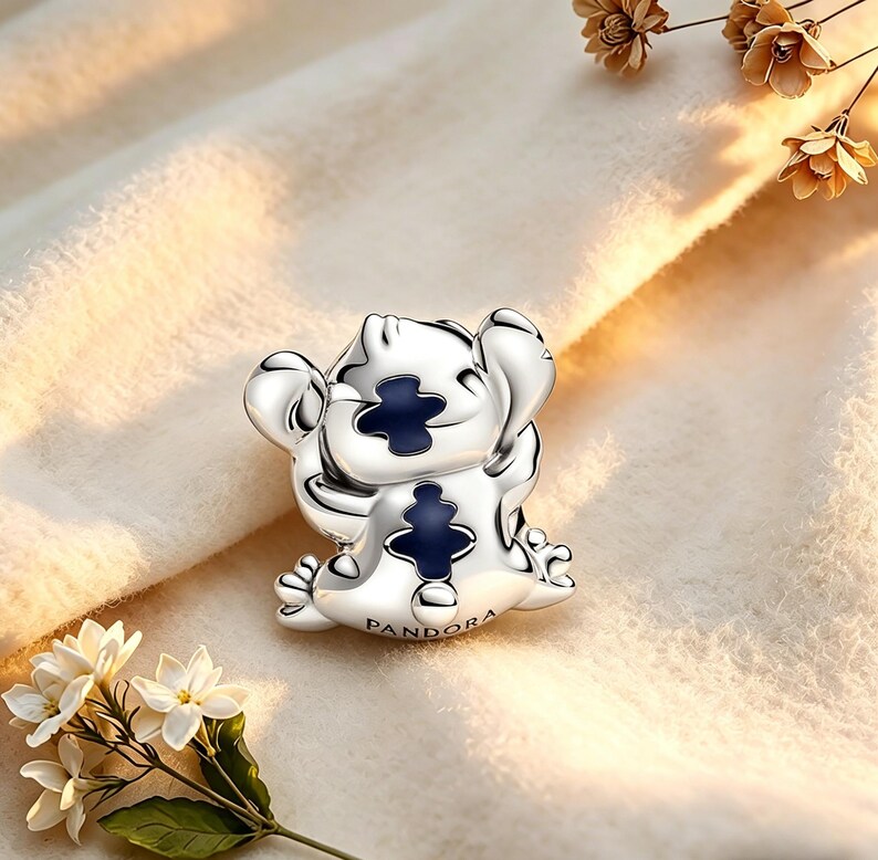 May include: A silver charm depicting a cartoon character with large ears and a blue chest detail. The charm has small feet and hands, and the word "PANDORA" is engraved on the base. The charm is set against a soft, neutral background.