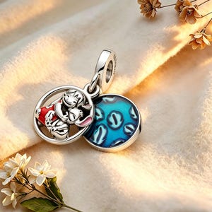 May include: A silver charm pendant with a cartoon character in a red outfit hugging a rabbit, set in a circular frame. It includes a blue enamel disc with a pattern. The charm is designed to be a pendant.