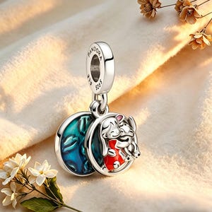 May include: A silver charm with the word "PANDORA" and "ALE 925" engraved. The charm features a round pendant with a blue and green design on one side and a cartoon elephant and mouse hugging on the other side, both in a circular frame.