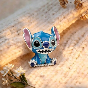 May include: A metal enamel pin featuring the character Stitch with bright blue skin, large ears with pink inner sections, and a wide grin showing white teeth. The character has large black eyes and a dark blue nose, rendered in a glossy finish.