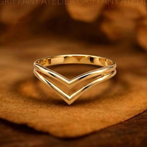 Peut inclure: Une bague en or poli présentant un design à double chevron ou en forme de V. La bague possède une surface lisse et réfléchissante ainsi qu'une structure métallique continue formant deux pointes distinctes dirigées vers le bas.