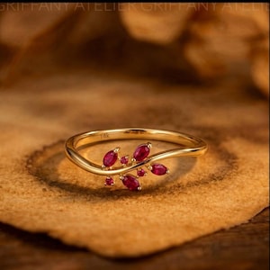 Könnte beinhalten: Ein goldener Ring mit einer zarten, geschwungenen Ringschiene und einer Anordnung aus kleinen, marquise- und rundgeschliffenen roten Rubinen in Blattform. Auf der Innenseite der Ringschiene ist deutlich der Text 14k zur Kennzeichnung eingeprägt.
