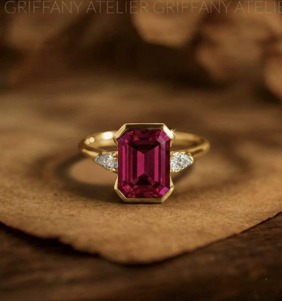 A magenta-red ruby in an emerald cut with pear diamond shoulders and 14K gold bezel — genuinely custom fine jewelry with solid demand (24 favorites).