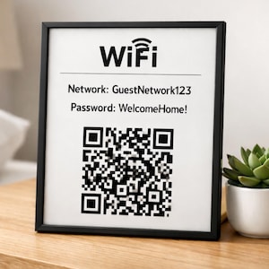 Könnte beinhalten: Schwarz gerahmtes WLAN-Schild mit Netzwerknamen und Passwort. Enthält einen QR-Code für einfachen Zugriff. Rechts vom Schild befindet sich eine kleine Sukkulente in einem weißen Topf. Das Schild steht auf einer Holzoberfläche.