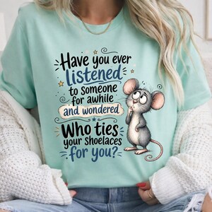 May include: A light mint green t-shirt featuring a cartoon mouse illustration and the text: Have you ever LISTENED to someone for awhile and wondered Who ties your shoelaces for you? The design includes small stars and decorative swirls.