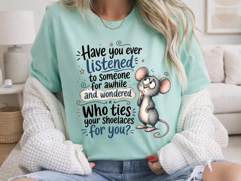 May include: A light mint green t-shirt featuring a cartoon mouse illustration and the text: Have you ever LISTENED to someone for awhile and wondered Who ties your shoelaces for you? The design includes small stars and decorative swirls.