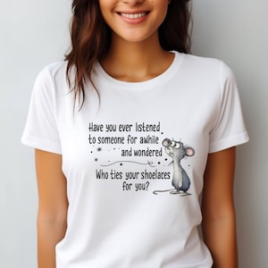 May include: White t-shirt featuring a cartoon mouse looking upwards with the text "Have you ever listened to someone for awhile and wondered Who ties your shoelaces for you?" The shirt has short sleeves.