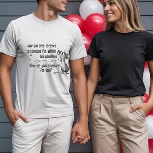 May include: A couple holding hands, each wearing a t-shirt. One shirt is white with a cartoon mouse and text: "Have you ever listened to someone for awhile and wondered Who ties your shoelaces for you?" The other shirt is black.