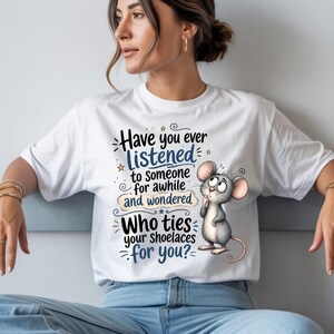 May include: A white short-sleeved t-shirt featuring a graphic of a grey mouse with large ears and a thoughtful expression. The text reads: Have you ever LISTENED to someone for awhile and wondered Who ties your shoelaces for you? with blue accents.