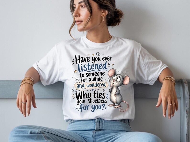 May include: A white short-sleeved t-shirt featuring a graphic of a grey mouse with large ears and a thoughtful expression. The text reads: Have you ever LISTENED to someone for awhile and wondered Who ties your shoelaces for you? with blue accents.