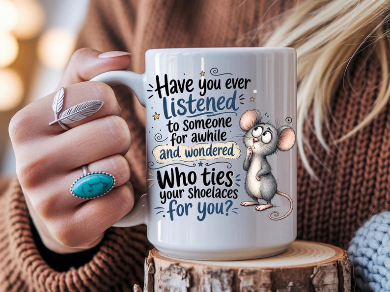 May include: A white ceramic mug featuring a cartoon illustration of a grey mouse and the text: Have you ever listened to someone for awhile and wondered Who ties your shoelaces for you? The mug has a handle and a smooth, glossy finish.