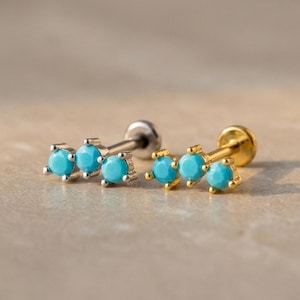 May include: Two pairs of stud earrings with three turquoise-colored stones each. One pair has silver-colored posts and settings, while the other has gold-colored posts and settings. The earrings are displayed on a neutral surface.
