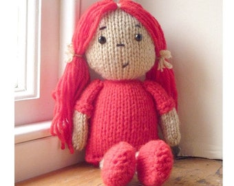 May include: A knitted doll with red hair, a red dress, and red shoes. The doll has a beige face with black eyes and a painted smile.