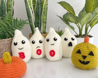 May include: A collection of handmade Halloween decorations, including knitted white ghosts with black eyes and red letter accents, and orange and yellow pumpkins. The ghosts have the letters "B" and "O" on them. The decorations are displayed on a white surface.