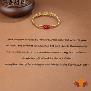 May include: A gold-colored bracelet with a red knot in the center. The bracelet is made of woven material and has a decorative design. The image also includes text about Tibetan Buddhism and the symbolism of colors.