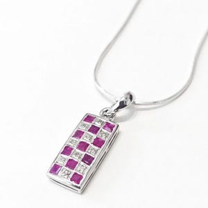 May include: A silver-toned necklace featuring a rectangular pendant with a checkerboard pattern of square-cut pink rubies and clear white diamonds. The pendant is suspended from a thin, flexible silver-toned chain that loops at the top.