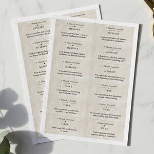 May include: Several printed cards with text, featuring phrases like "Memory" and "Care," are arranged on a marble surface. The cards have a vintage aesthetic with a beige background and dark text. Gold scissors are in the background.