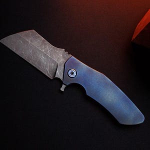 May include: A small, gray cleaver-style knife with a blue handle. The blade has a textured finish and a straight edge. The handle is a gradient of blue hues. The knife is set against a dark background.