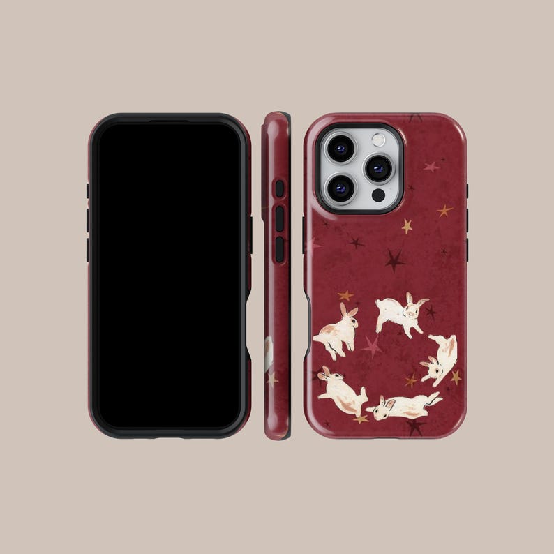 May include: A burgundy phone case featuring a whimsical design of white and brown rabbits in a circle, with scattered gold stars. The case is shown from multiple angles, including the front, side, and back.