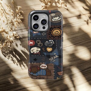 Puede incluir: Una funda de teléfono con un diseño de patchwork que presenta varias ilustraciones de dibujos animados. La funda tiene un fondo similar al denim con parches marrones, negros y azules. Los parches incluyen una taza de café, una carita sonriente, un gato, un perro y la palabra "STAR."