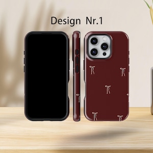 May include: Three phone cases are displayed. The front of the phone case is black, the side is maroon, and the back is maroon with a pattern of small, light-coloured bows. The text "Design Nr.1" is at the top.