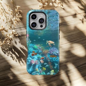 May include: A phone case featuring a vibrant underwater scene. The design includes a sea turtle, colorful coral, and various fish. The case has a glossy finish and a blue and teal color scheme.