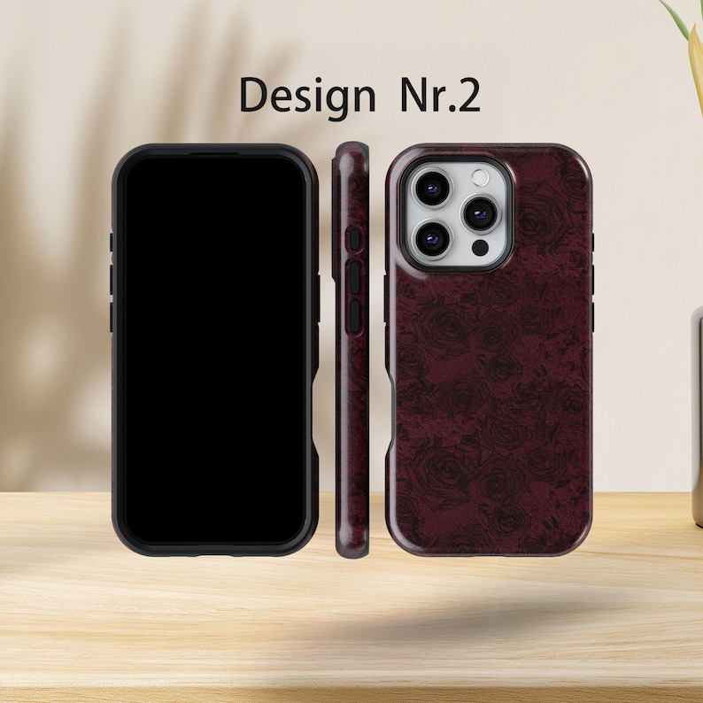 May include: Three phone cases are displayed. One is black, showing the phone screen. The second is a side view of a burgundy case. The third is a burgundy case with a rose pattern and the text "Design Nr.2".