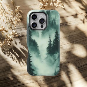 May include: A phone case featuring a misty forest design. The case has a dark green and white color scheme with a detailed illustration of trees and fog. The case is designed to fit a smartphone and has a protective bumper.