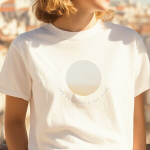 Könnte beinhalten: Weißes T-Shirt mit einem kreisförmigen Grafikdesign mit einem Gelb-Weiß-Verlauf und dem Text "THE GOOD DAYS ARE HERE" in einem Halbkreis um die Grafik. Das T-Shirt hat kurze Ärmel.