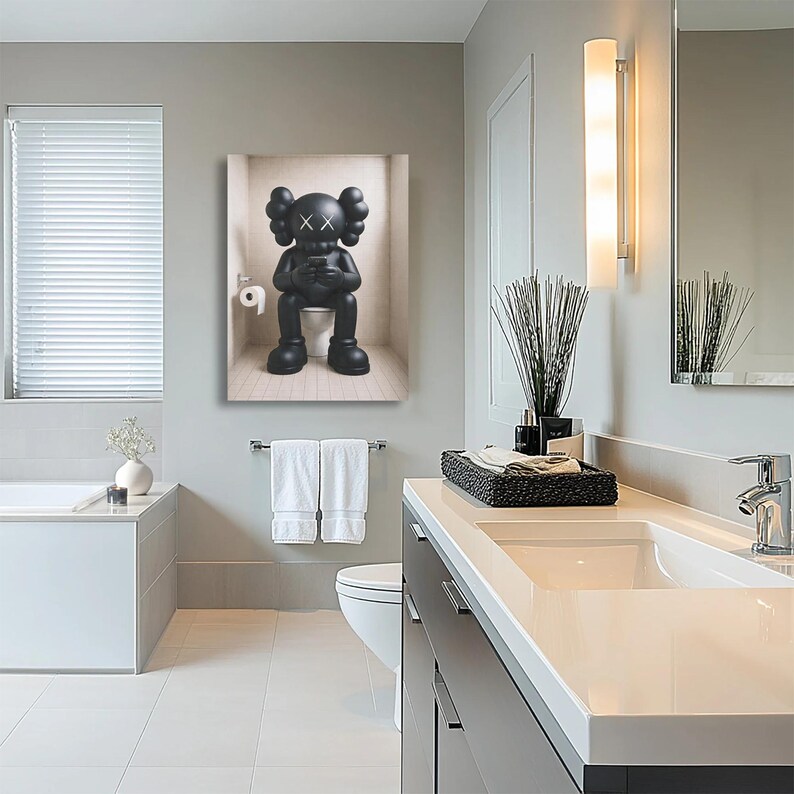 May include: A rectangular wall art print featuring a black KAWS character sitting on a toilet while looking at a smartphone. The character has signature X-shaped eyes and rounded ears. A roll of white toilet paper is mounted on the wall beside it.