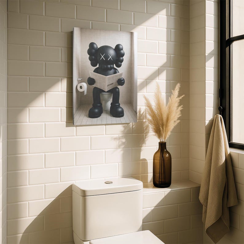 May include: A rectangular wall art print featuring a black KAWS character sitting on a toilet while reading a newspaper. The character has signature X-shaped eyes and rounded ears. A white toilet paper roll is mounted on the wall beside the figure.