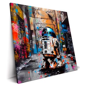 Peut inclure: Impression sur toile représentant R2-D2 dans une ruelle couverte de graffitis. L'œuvre présente le droïde emblématique avec une tête bleue et un corps blanc et orange, sur fond de street art vibrant aux tons orange, rose et bleu.
