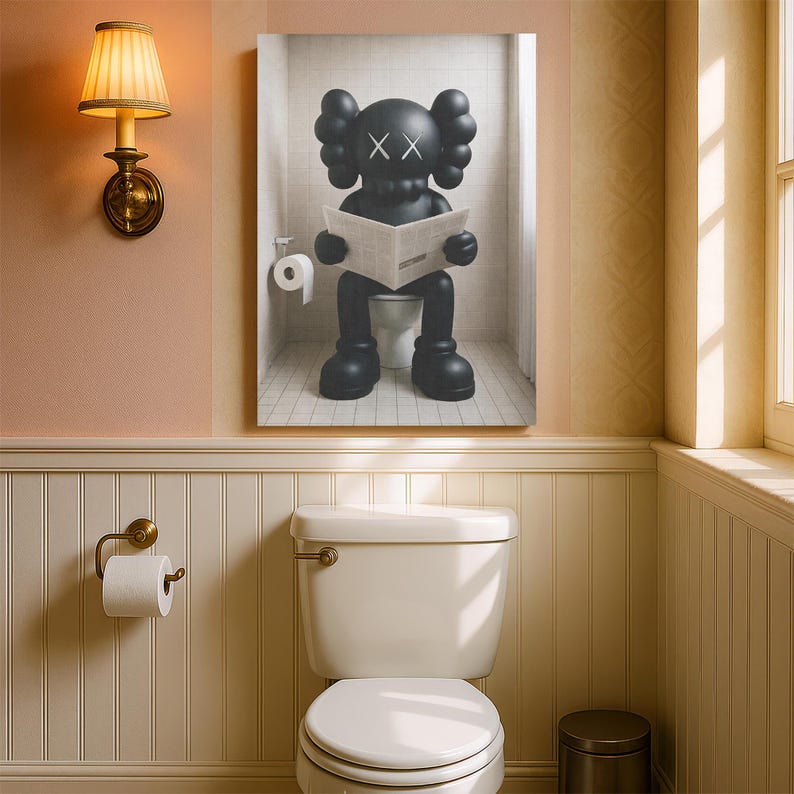 May include: A framed wall art print depicting a black KAWS-style character with X-shaped eyes sitting on a white toilet in a tiled bathroom, reading a newspaper. The character has rounded ears and large hands, positioned centrally within the frame.