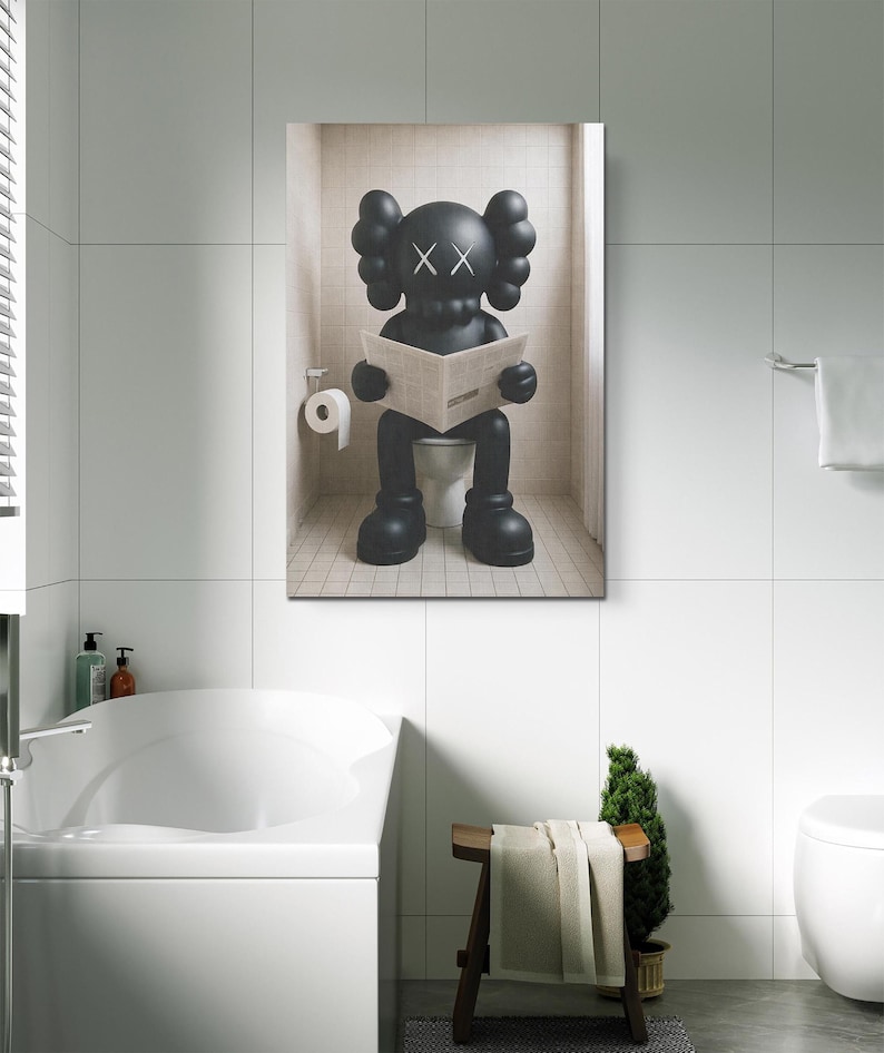 May include: A rectangular wall art print featuring a black KAWS character with X-shaped eyes sitting on a white toilet in a tiled bathroom. The character is holding an open newspaper. A roll of white toilet paper is mounted on the wall to the left.