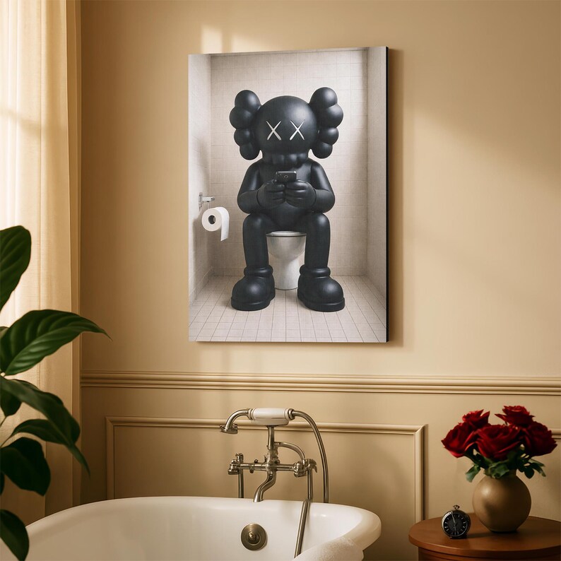 May include: A framed wall art print depicting a matte black KAWS character with X-shaped eyes sitting on a white toilet in a tiled bathroom. The character holds a small black device in its hands, and a roll of white toilet paper hangs on the wall.
