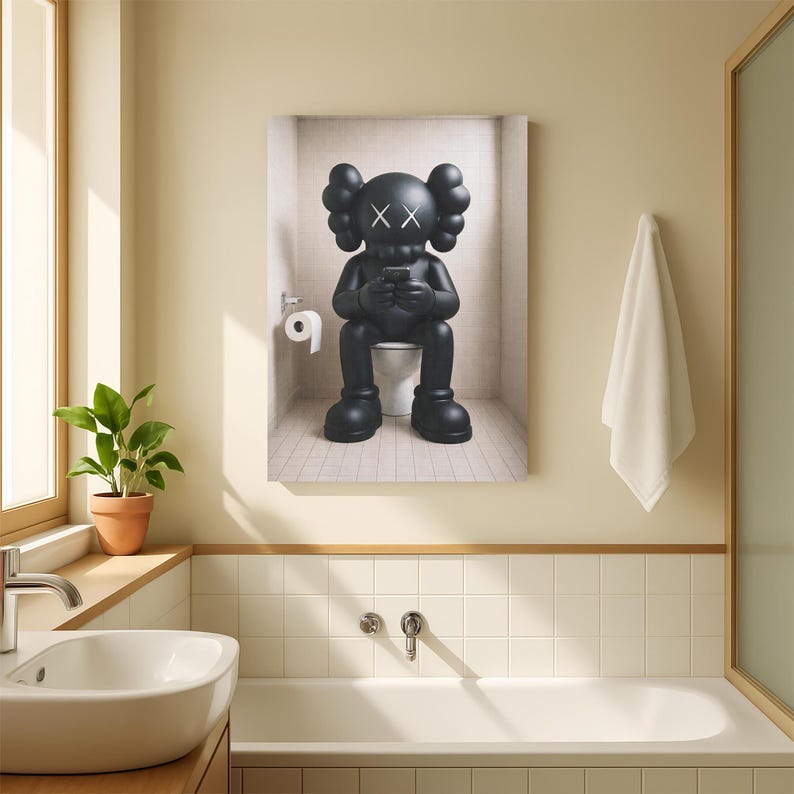May include: A rectangular wall art print featuring a black cartoon character with X-shaped eyes sitting on a white toilet in a tiled bathroom, holding a small black device. A white toilet paper roll is mounted on the wall to the left of the figure.
