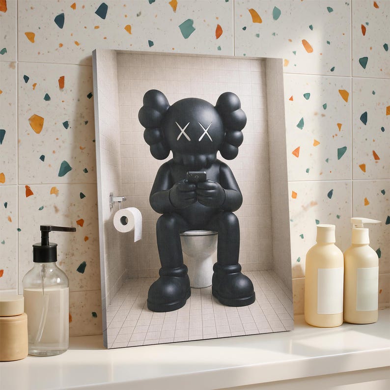 May include: A rectangular wall art print featuring a black cartoon character with X-shaped eyes sitting on a white toilet in a tiled bathroom, holding a small black smartphone, with a white toilet paper roll mounted on the wall to the left.