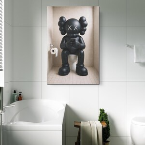 May include: A black KAWS character figurine with X-shaped eyes sitting on a white toilet while holding a small rectangular device. The figure has large rounded ears and oversized feet, positioned in a tiled alcove with a toilet paper roll holder.