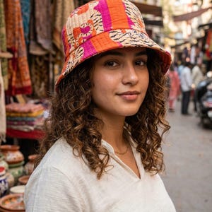 May include: A quilted bucket hat featuring a vibrant pattern of orange, pink, and black tiger stripes. The hat has a downward-sloping brim and a stitched texture throughout, showcasing a bold color palette and a distinct animal-inspired print design.