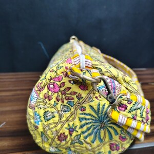 Puede incluir: Bolsa de deporte amarilla con estampado floral y dise&ntilde;o acolchado. La bolsa presenta un patr&oacute;n vibrante de flores y follaje rosas, azules y verdes sobre un fondo amarillo. Tiene una cremallera blanca y una correa para el hombro desmontable con rayas amarillas y blancas.